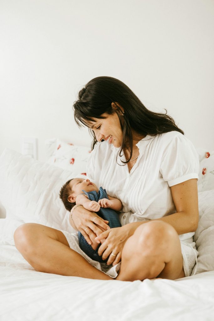 A mother lovingly cradles her baby in a serene bedroom setting.